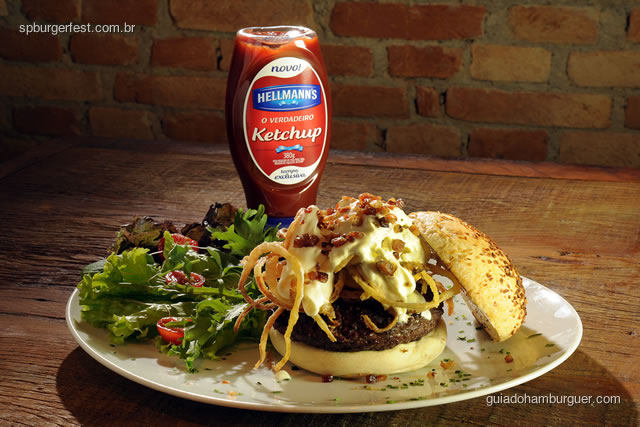 Vincent Vega - hambúrguer de 250 gramas recheado de muçarela e bacon, coberto por sour cream salpicado de bacon bits e crispy onions, servido no pão de cebola. Acompanha salada no prato. - SP Burger Fest 3ª edição