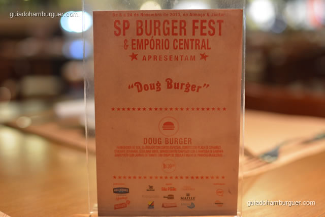 Doug Burger – suculento hambúrguer de 180g, elaborado com cortes especiais, coberto com placa de caramelo crocante defumado, perfumado com cebolinaha verde, servido em pão chapeado com a legitima manteiga de garrafa sobreposto sobre laminas de tomate com crispy de cebola e delicioso molho de pimentas brasileiras  - Empório Central