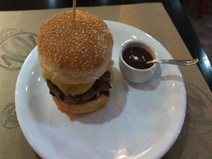 Hambúrguer de costelinha de porco, com aproximadamente 2cm de altura, juntamente com queijo prato derretido e cebola caramelada e acompanhado de molho barbecue por R$ 19,50 - Hamburgueria 162